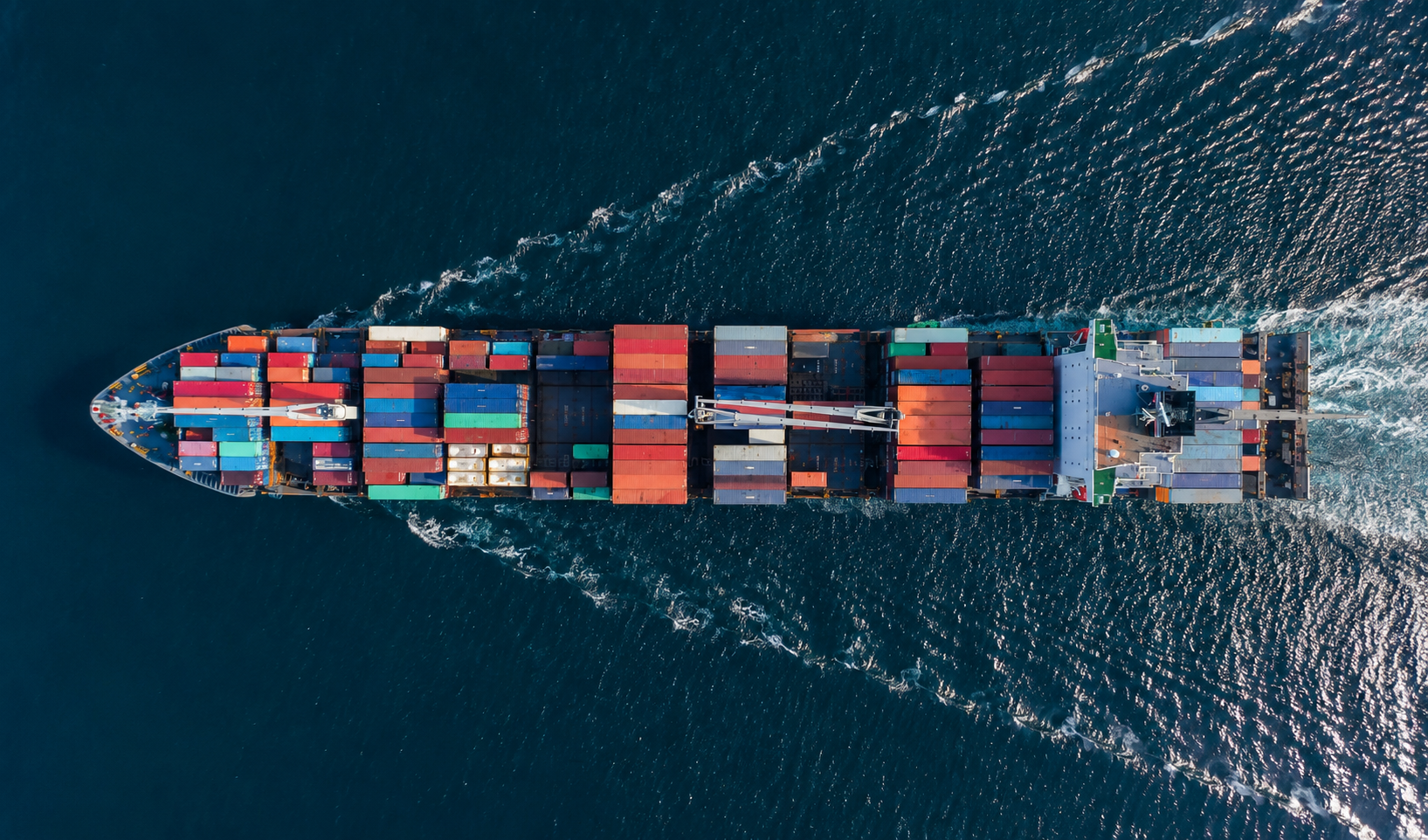 Top-down aerial view of a fully loaded container ship cutting through dark ocean water