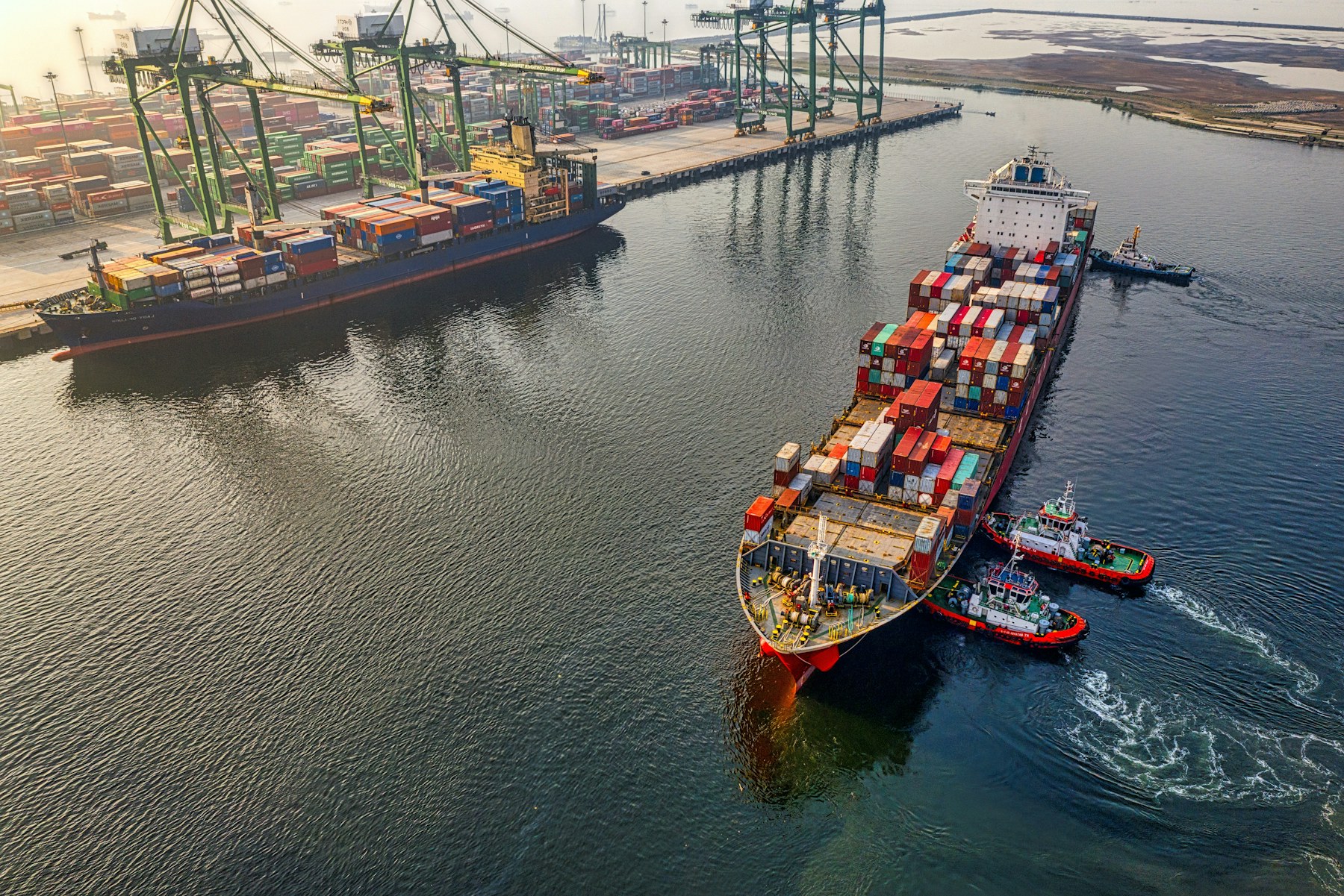 Container ship guided by tugboats entering a busy commercial port